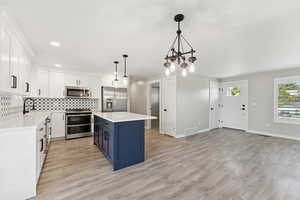 Kitchen with stainless steel appliances, backsplash, white cabinets, light countertops, and blue cabinets