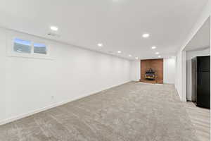Basement with freestanding refrigerator, a fireplace, recessed lighting, and light colored carpet