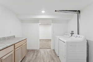 Washroom featuring washing machine and dryer, light wood-style flooring, cabinet space, and recessed lighting