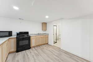 Kitchen featuring light brown cabinets, black appliances, light wood-type flooring, light countertops, and recessed lighting