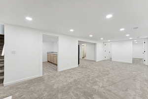 Finished below grade area featuring stairs, light colored carpet, and recessed lighting