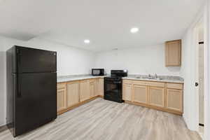 Kitchen featuring light brown cabinetry, black appliances, light wood-style flooring, light countertops, and recessed lighting