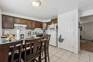 Kitchen with white appliances, dark brown cabinetry, light tile patterned floors, light countertops, and a textured ceiling