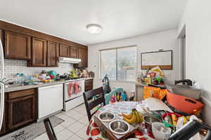 Kitchen with white appliances, light countertops, backsplash, under cabinet range hood, and dark brown cabinetry