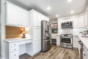 Kitchen with appliances with stainless steel finishes, white cabinets, light countertops, light wood-style flooring, and decorative backsplash