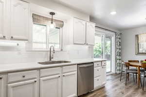 Kitchen featuring tasteful backsplash, decorative light fixtures, dishwasher, white cabinetry, and light wood-style floors