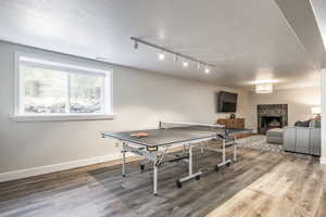 Recreation room with a tiled fireplace, a textured ceiling, light wood-type flooring, and track lighting