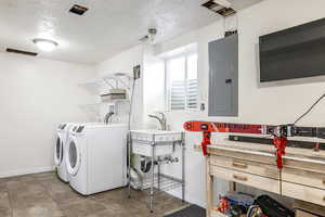 Laundry area with a textured ceiling, electric panel, and washing machine and dryer