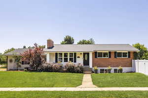Ranch-style home with a chimney, covered porch, brick siding, and a shingled roof