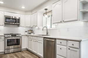 Kitchen featuring appliances with stainless steel finishes, decorative light fixtures, white cabinetry, open shelves, and recessed lighting