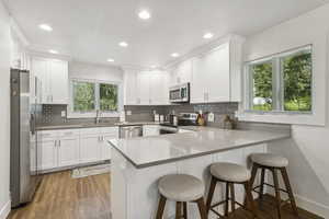 Kitchen featuring a peninsula, stainless steel appliances, backsplash, white cabinets, and recessed lighting