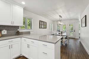 Kitchen with a peninsula, a chandelier, white cabinetry, dark wood-type flooring, and a textured ceiling