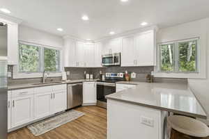 Kitchen with a peninsula, stainless steel appliances, white cabinets, wood finished floors, and decorative backsplash