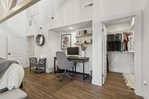 Bedroom with a spacious closet, dark wood-type flooring, a desk, and a high ceiling