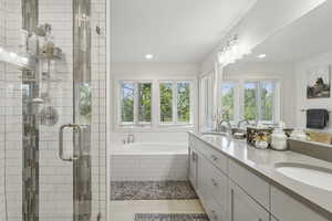 Full bath with healthy amount of natural light, double vanity, a bath, a stall shower, and recessed lighting