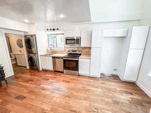 Kitchen featuring stacked washer / dryer, stainless steel appliances, a textured ceiling, white cabinets, and light countertops