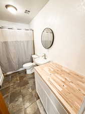 Full bathroom featuring a textured wall, a textured ceiling, vanity, stone finish flooring, and a shower with curtain