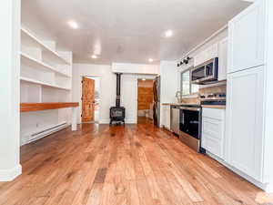 Kitchen featuring a wood stove, stainless steel appliances, baseboard heating, light wood-type flooring, and white cabinets
