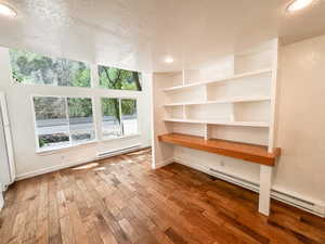 Unfurnished office featuring a textured ceiling, a baseboard heating unit, wood finished floors, and recessed lighting