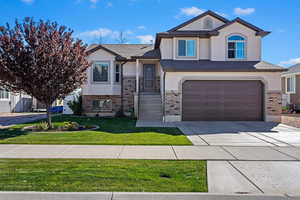 View of front of property with stucco siding, an attached garage, brick siding, and a front lawn