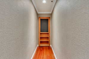 Corridor with light wood-style flooring, ornamental molding, recessed lighting, and a textured wall
