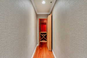 Corridor with light wood-type flooring, ornamental molding, recessed lighting, and a textured wall