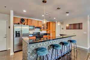 Kitchen with stainless steel appliances, dark countertops, a kitchen breakfast bar, recessed lighting, and a center island with sink