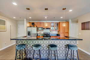 Kitchen featuring dark countertops, dark tile patterned flooring, appliances with stainless steel finishes, a kitchen bar, and recessed lighting