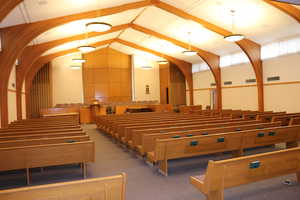 View of chapel with rows of wood pews and raised dais