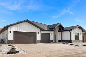 Modern farmhouse style home featuring stone siding, a garage, board and batten siding, and driveway