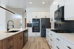 Kitchen featuring black appliances, light wood-style floors, light countertops, tasteful backsplash, and recessed lighting