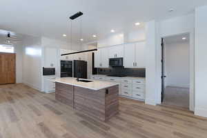 Kitchen featuring light wood-style flooring, tasteful backsplash, light countertops, a kitchen island with sink, and black appliances