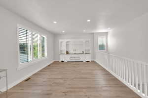 Open living room with recessed lighting, light wood-style flooring, with banister, and lots of natural light.