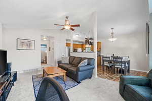 Living room with lofted ceiling, ceiling fan, and light colored carpet