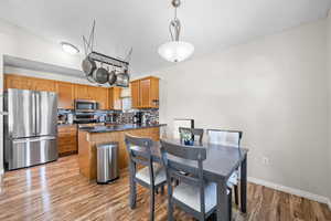 Kitchen with appliances with stainless steel finishes, a peninsula, brown cabinets, dark countertops, and backsplash