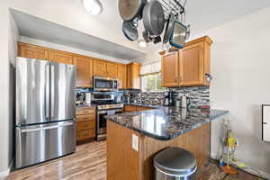 Kitchen with appliances with stainless steel finishes, brown cabinetry, a peninsula, decorative backsplash, and lofted ceiling