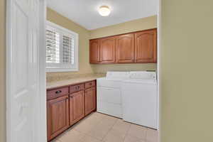 Laundry area with cabinet space, washer and dryer, and light tile patterned floors