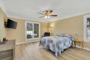 Bedroom featuring wood finished floors, multiple windows, ornamental molding, and ceiling fan