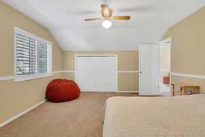 Carpeted bedroom featuring vaulted ceiling, a closet, and ceiling fan
