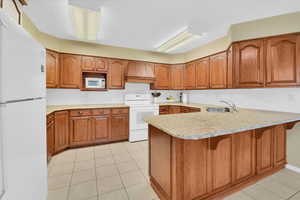 Kitchen with white appliances, a peninsula, light tile patterned floors, and brown cabinetry