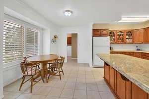 Kitchen featuring freestanding refrigerator, brown cabinetry, glass insert cabinets, light tile patterned floors, and washer / clothes dryer