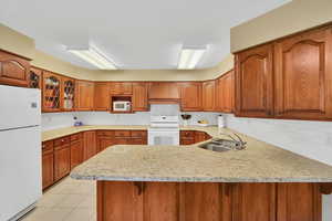 Kitchen featuring white appliances, a peninsula, custom exhaust hood, and brown cabinets