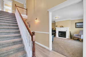 Stairway featuring crown molding, a fireplace with flush hearth, wood finished floors, and carpet