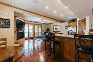Kitchen with ornamental molding, brown cabinetry, stainless steel refrigerator with ice dispenser, a kitchen bar, and a ceiling fan