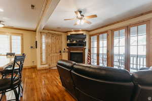 Living area featuring ornamental molding, a glass covered fireplace, light wood-type flooring, ceiling fan, and french doors