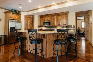 Kitchen featuring appliances with stainless steel finishes, dark wood-style floors, crown molding, tasteful backsplash, and light stone counters