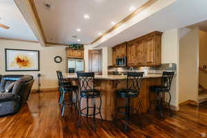Kitchen featuring light stone countertops, brown cabinets, a peninsula, dark wood finished floors, and ornamental molding