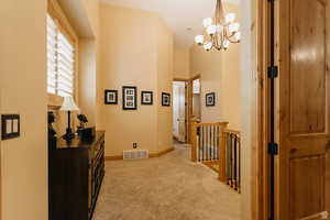 Hallway featuring light carpet, an upstairs landing, and a chandelier