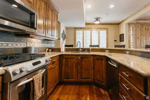 Kitchen featuring stainless steel appliances, dark wood finished floors, light stone counters, tasteful backsplash, and crown molding