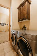 Laundry area with cabinet space, washing machine and clothes dryer, light colored carpet, and light tile patterned floors